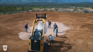 Crew spreading dry sodium bentonite over compacted soil to build a pond.